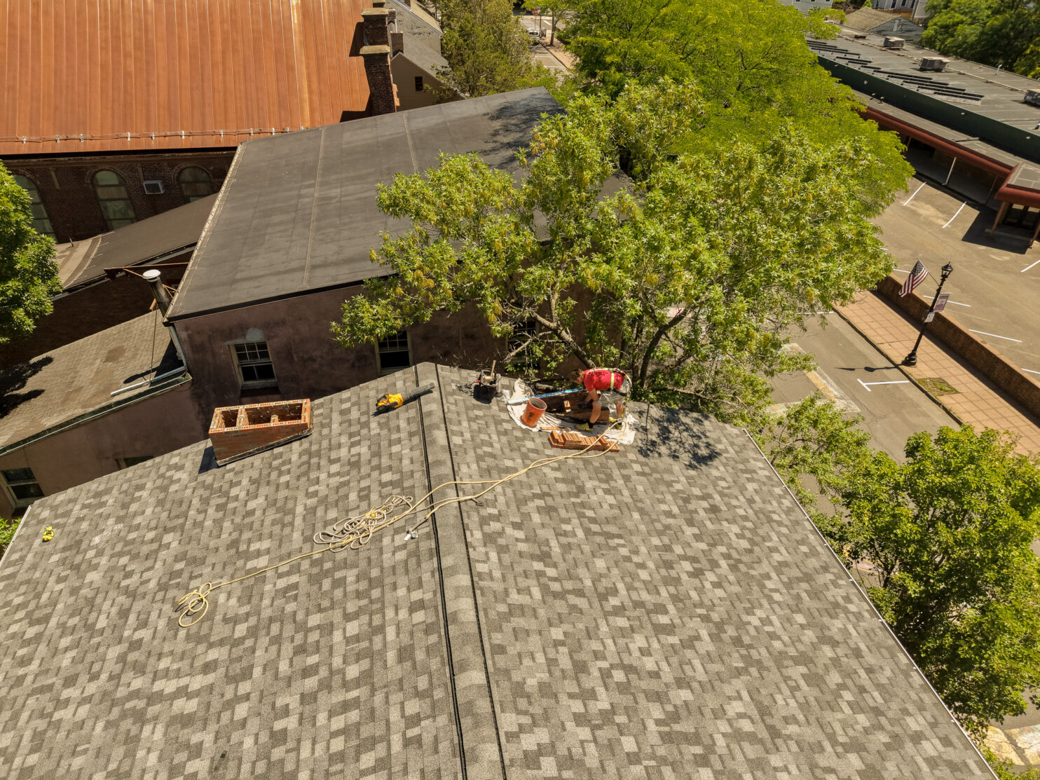 Home Evolution Roofing technician on a shingle roof starting a chimney rebuild with the old stack taken down to the base