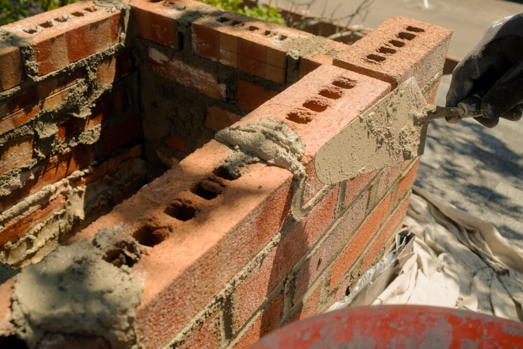 Overhead view of a roofer applying mortar while laying new brick during a chimney rebuild in Columbia County NY