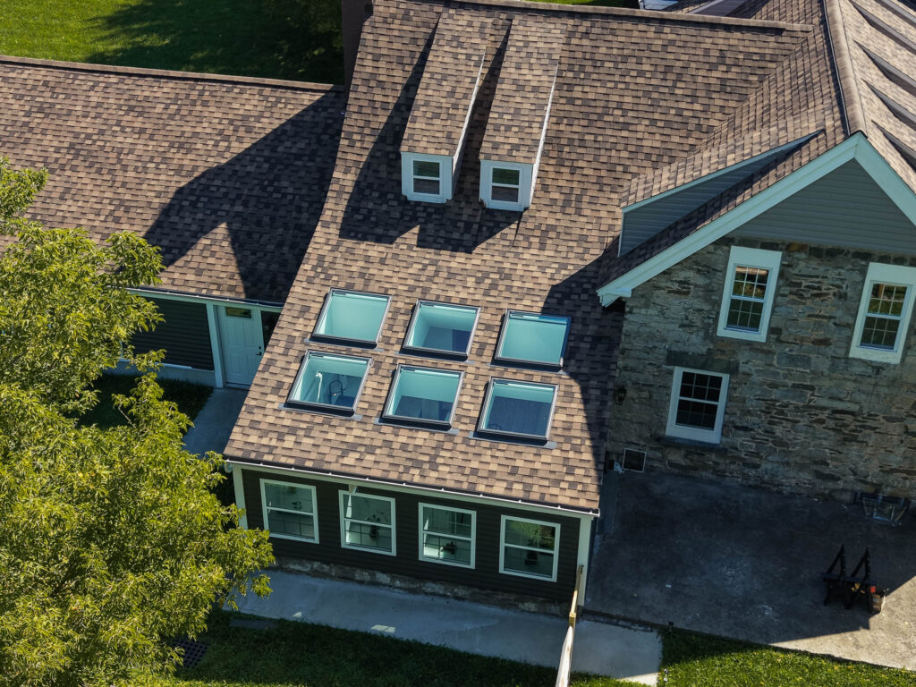 Six VELUX skylights above a sunroom next to original stone wall on a historic Hudson Valley farmhouse